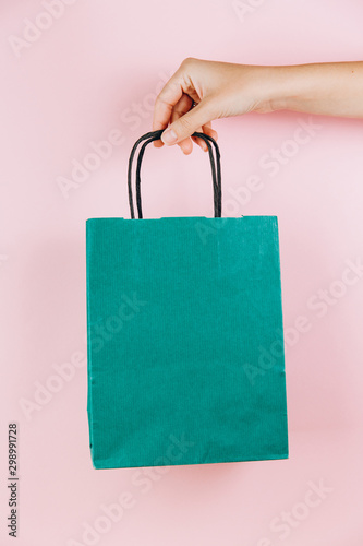 Female hand holding green paper bag isolated on pink background