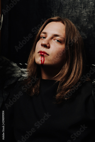 young long hair caucasian guy is going to go to a Halloween party in with makeup of blood from his mouth © goldeneden
