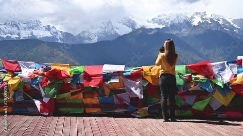 Young woman photographer taking photographs of Meili snow mountain infront tibetan buddhist prayer flags in Yunnan, China