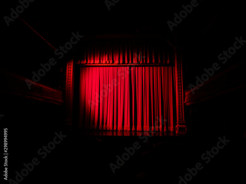 Red velvet curtains drawn across the screen and stage in a darkened old vintage cinema / theatre