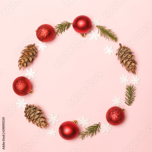 Red Christmas shiny balls and fir twigs on pale pink background. Christmas ornaments arrangement with copy space.