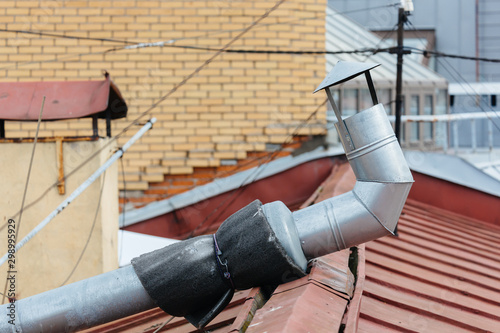 Close up photo ventilation pipe from stainless steel on red rooftop. The ventilation system of a residential building. Inox chimney with exhaust fan. Selective focus.