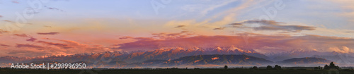 Panorama. Fairytale dawn, sunset with bright multi-colored clouds, against the backdrop of a mountain range with snow-capped peaks
