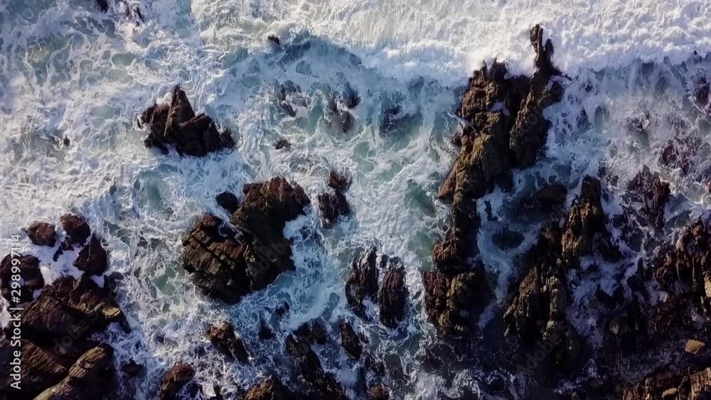 Large and powerful waves cover the rocky coast of the Atlantic Ocean. View from drone on large stones. Huge waves break on a cliff and sea white foam forms. The strength and power of the ocean