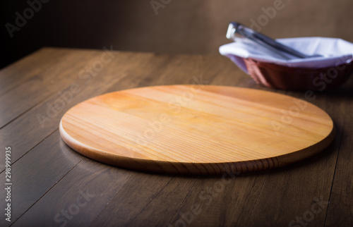 Round wooden board on a wooden table used to serve pizza. Background blur a basket with napkin and holder. Horizontal photo with blurred background. photo