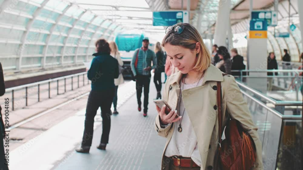 Young Woman Using Smartphone and Waiting for Train at a Railway Station. SLOW MOTION. Girl texting on a Cell Phone while waiting for a train. Technology in everyday life and travel.