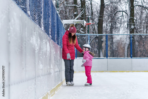 Mom teaches her little daughter to skate on the rink on a winter day. Weekends activities outdoor in cold weather. photo