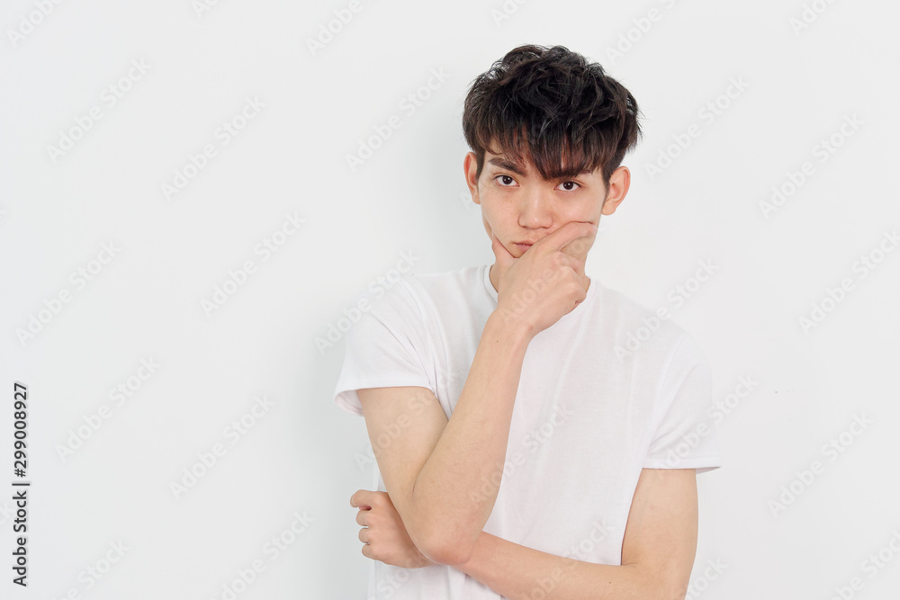Portrait of a handsome Chinese young man in white t shirt looking at camera with hand covering his mouth, thoughtful expression, isolated on white background. Portrait of a handsome Chinese young man in white t shirt looking at camera with hand covering his mouth, thoughtful expression, isolated on white background.