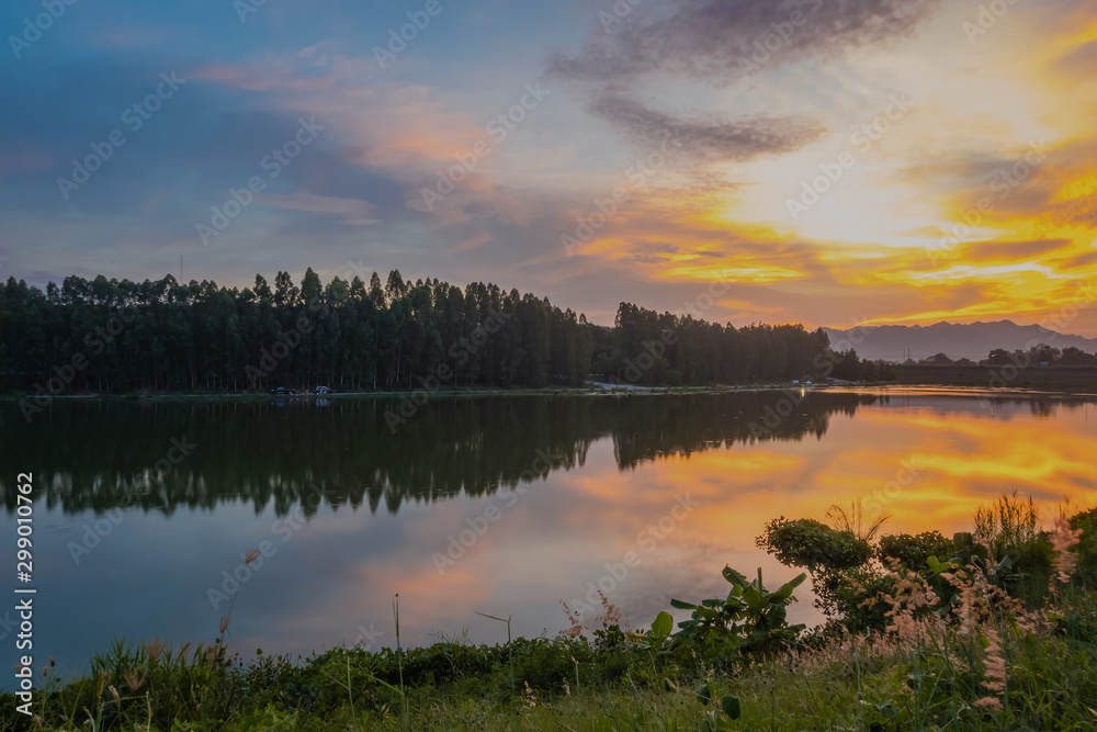 Beautiful view of twilight silhouette sunset on the water reservoir while the sky after sunset has orange light coming out of the clouds and reflecting with the water in the reservoir. Beautiful view of twilight silhouette sunset on the water reservoir while the sky after sunset has orange light coming out of the clouds and reflecting with the water in the reservoir.