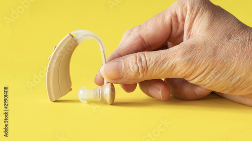 Hand holding hearing aid on yellow background ,high technological treatment device for hearing improvement to  person with hearing loss