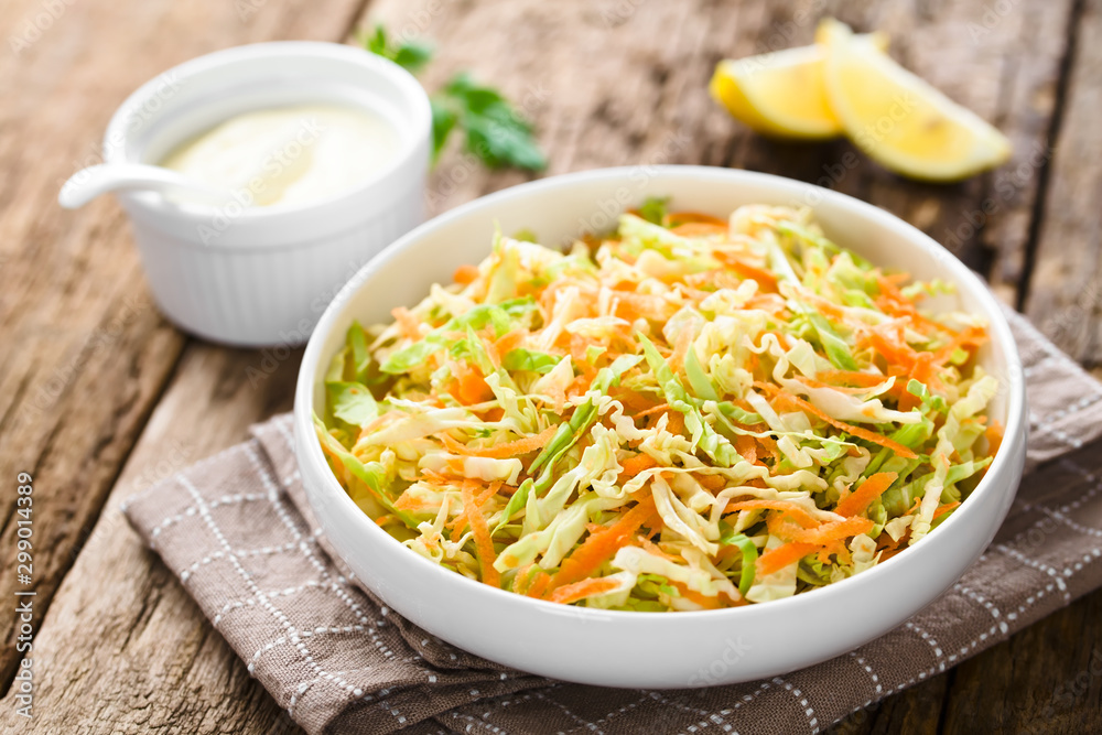 Coleslaw made of freshly shredded white cabbage and grated carrot in bowl, homemade mayonnaise-based salad dressing and lemon wedges in the back (Selective Focus, Focus in the middle of the salad) Coleslaw made of freshly shredded white cabbage and grated carrot in bowl, homemade mayonnaise-based salad dressing and lemon wedges in the back (Selective Focus, Focus in the middle of the salad)
