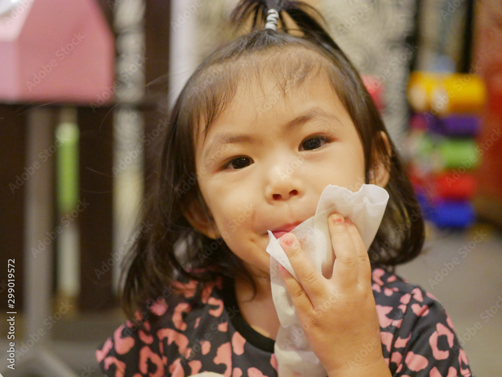 Little baby girl holding and using a baby wipe to clean her lips by herself
