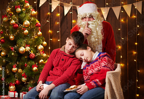 The children waited a long time for Santa, now they fell asleep and Santa quietly goes to the Christmas tree to give presents - Merry Christmas and Happy Holidays! © soleg