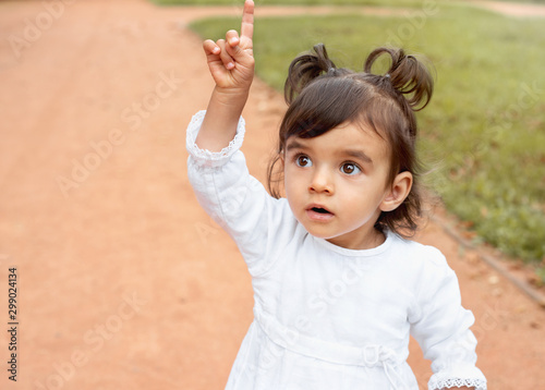 Little amazed baby girl pointing finger up in the park