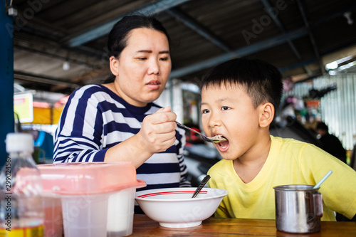 Asian mother feeding her son in noodle food shop