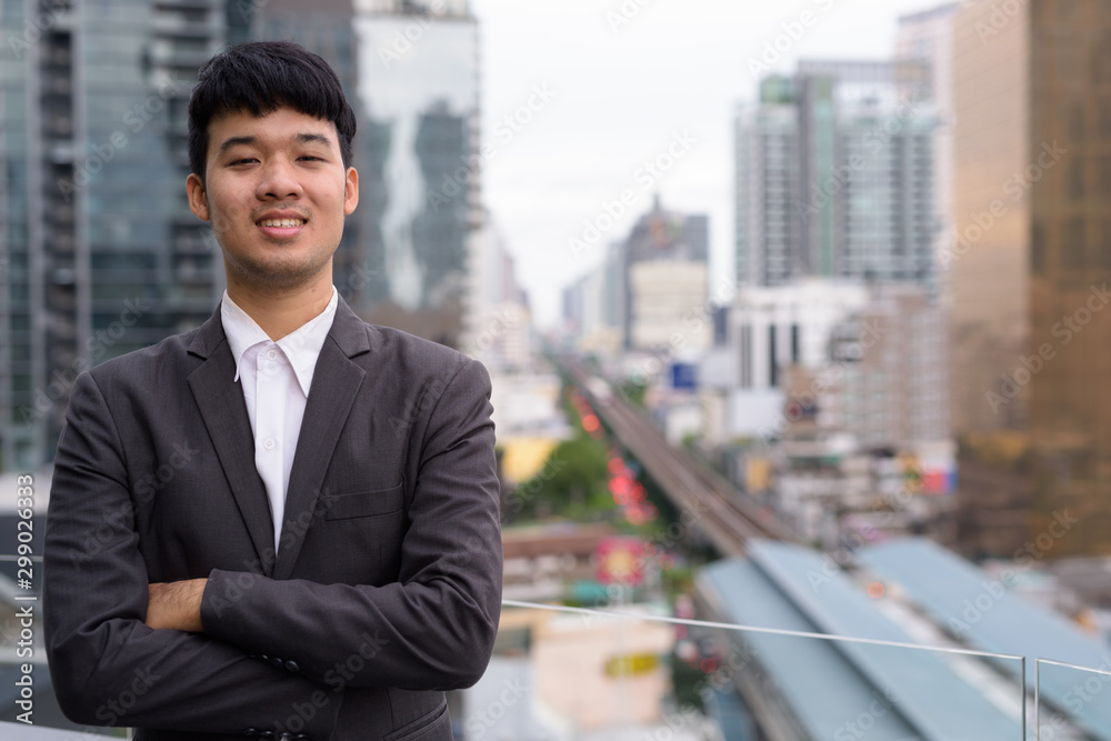 Portrait of young Asian businessman against view of the city Portrait of young Asian businessman against view of the city