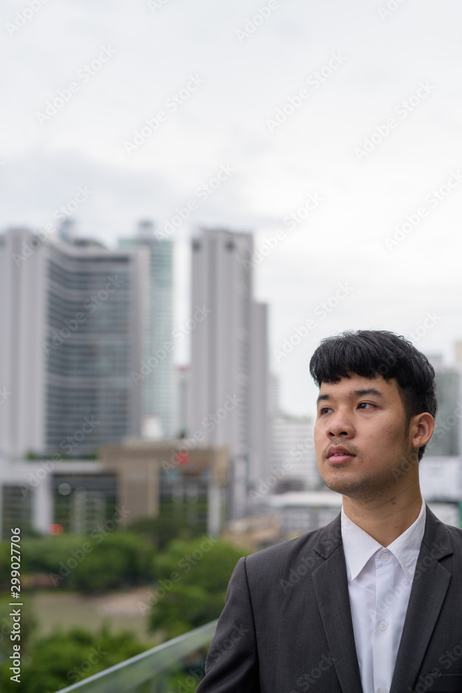 Portrait of young Asian businessman against view of the city Portrait of young Asian businessman against view of the city