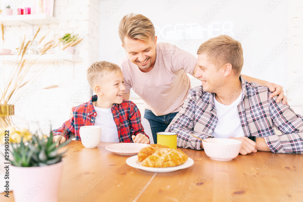 Happy young fathers and son have breakfast in the kitchen, gay family with a child, time together, parenting in homosexual families concept