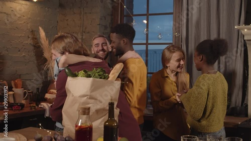 Tracking shot of happy people smiling and hugging guests arriving to dinner party in their apartment. They are chatting and thanking their friends for bringing groceries