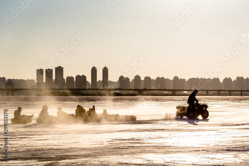 Silhouette of Winter river the turns into frozen, People can walk down and arrange activities on the river, The ATV car pull a person sitting on the rubber ring around the river in Harbin China. photo