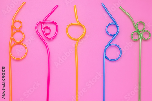 Plastic spiral multicolor tubes on pink paper card. Abstract colorful background of curved cocktail straws. Laconic design. Concept of fun mood. Modern style. 