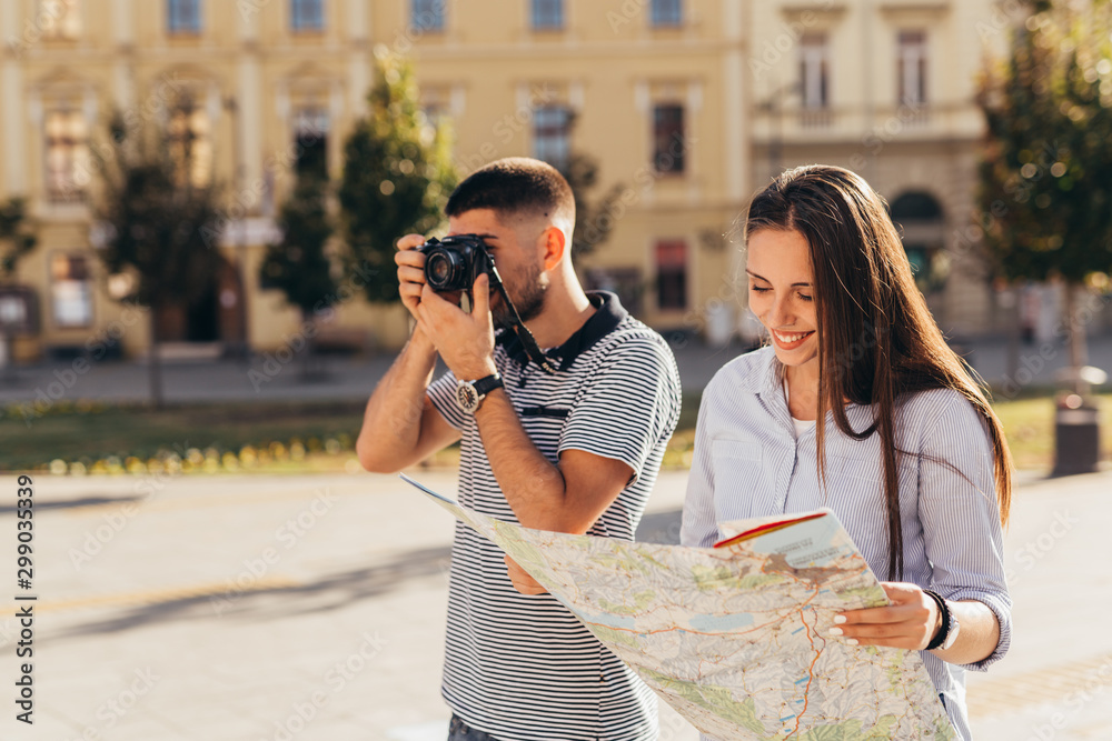 young tourists exploring town using map and taking picture with camera