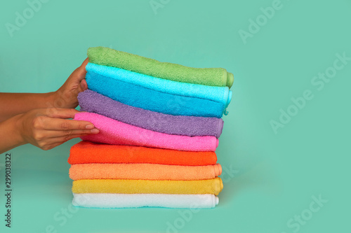 Close-up of hands putting stack of fresh bath towels. stack of multi-colored clean towels on a blue background