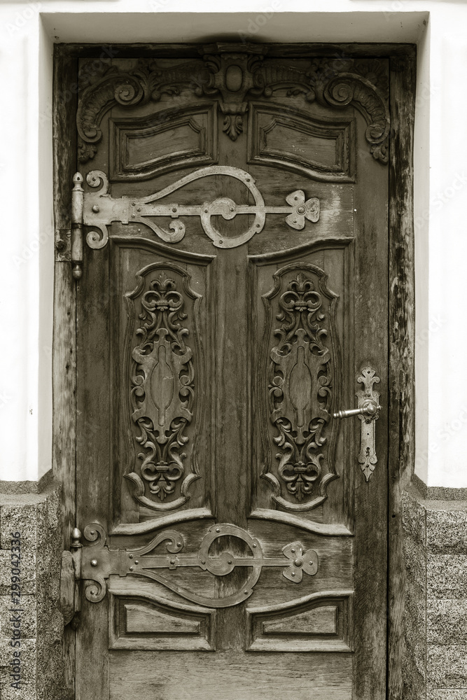 The old wooden door. Ancient antique wooden in an old wall. Ancient decorative wooden door. Historical art style facade of an elite expensive antique door. Wooden background, vintage element