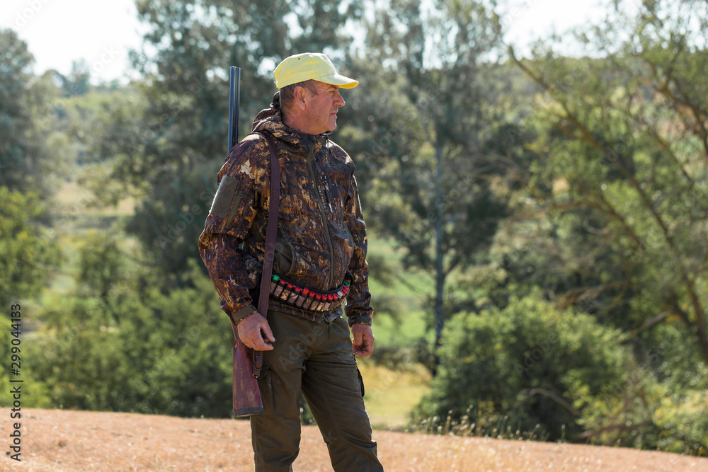 Hunting period, autumn season open. A hunter with a gun in his hands in hunting clothes in the autumn forest in search of a trophy. A man stands with weapons and hunting dogs tracking down the game. Hunting period, autumn season open. A hunter with a gun in his hands in hunting clothes in the autumn forest in search of a trophy. A man stands with weapons and hunting dogs tracking down the game.
