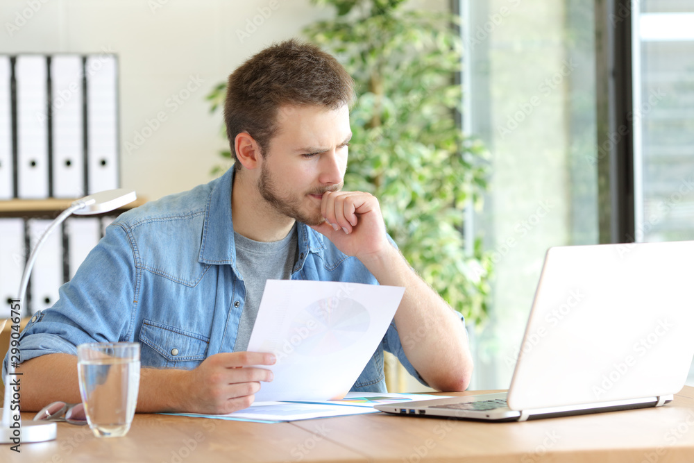 Pensive man holding document reading laptop content Pensive man holding document reading laptop content