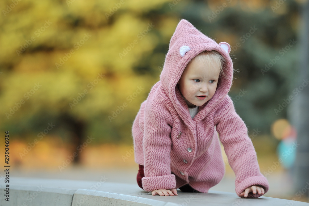 Little cute girl blond child 3-4 years old in a knitted coat crawls on arms and legs, on all fours while walking in the autumn park Little cute girl blond child 3-4 years old in a knitted coat crawls on arms and legs, on all fours while walking in the autumn park