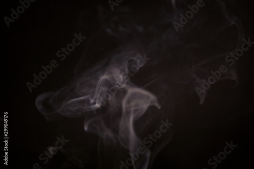White steam spins and rises from the pan. White smoke rises from a large pot, which is located behind the frame. black background. Texture of smoky cloud