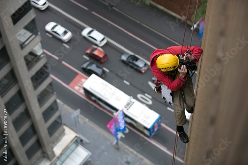 Rope access engineer rappelling, working at height, inspection taking picture of building structure leak for further report high rise construction building site Sydney, city skyline, Australia 