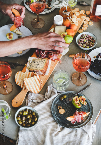 Mid-summer picnic with wine and snacks. Charcuterie and cheese board, rose wine, nuts, olives, fresh fruits and mans hands holding food over concrete table background