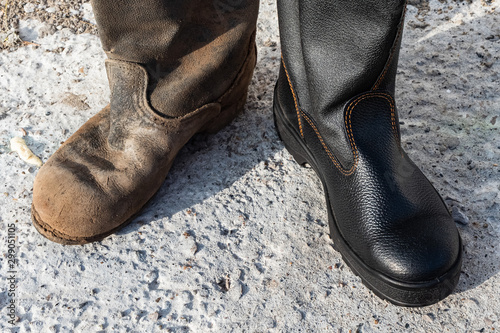 A pair of different boots. Contrast old and new, clean and dirty shoes close-up.