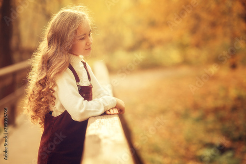 girl standing at the railing of wooden bridge standing in the park at daytime, side view