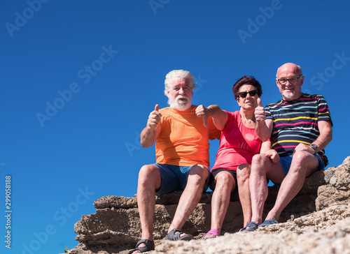 Senior caucasian people sitting on the cliffs smiling and gesturing up and down. Enjoying free time and retirement.