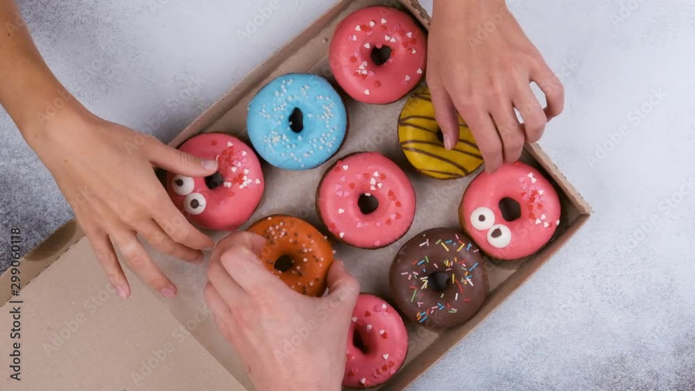 Top view of delicious sweet donuts. People take donuts out of the box on a wooden table background, slow motion.