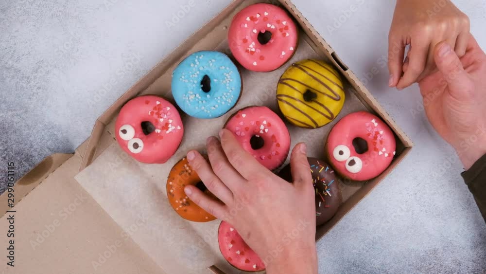 Top view of delicious sweet donuts. Loving couple at a meeting on Valentine's Day take donuts out of the box on a grey table background, slow motion.