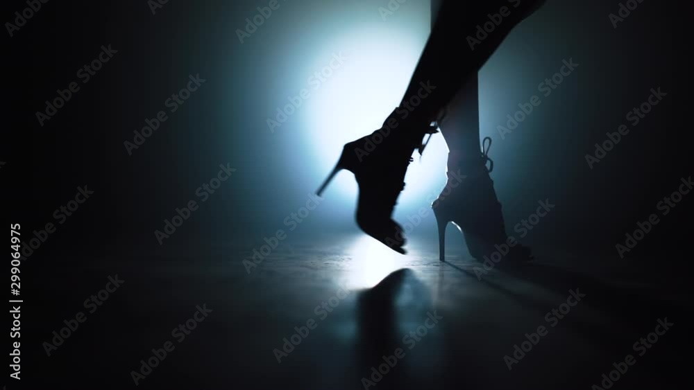Woman in heels walks near camera across spotlight on smoky stage. Girl in sexy clothing. Nightclub dancer concept.