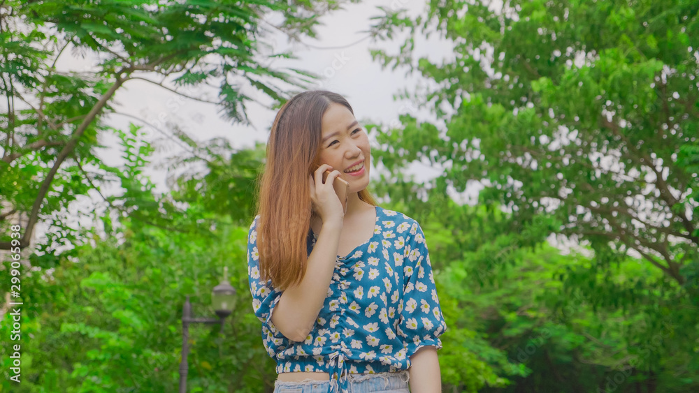 Asian girl smiling enjoying using a smartphone at a park with a green tree. Happy woman. Asian girl smiling enjoying using a smartphone at a park with a green tree. Happy woman.