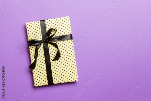 Gift box with black bow for Christmas or New Year day on purple background, top view with copy space