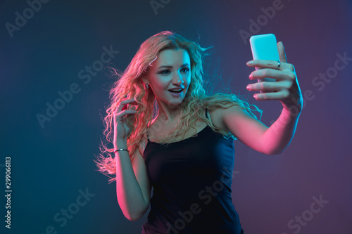 Caucasian young woman's portrait on gradient background in neon light. Beautiful female model with unusual look. Concept of human emotions, facial expression, sales, ad. Making selfie, bet, purchases. © master1305