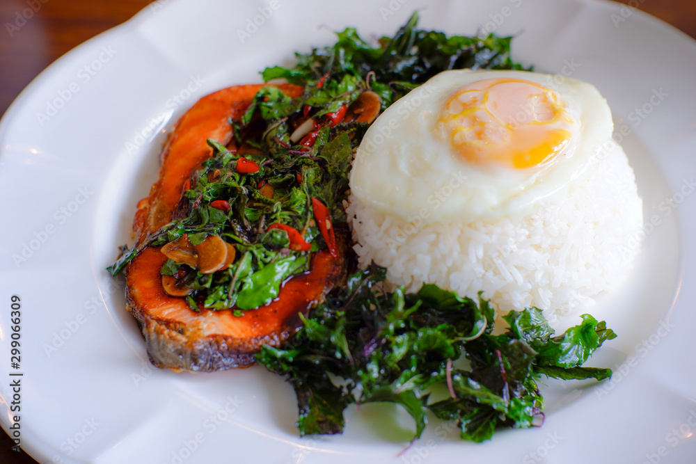 Grilled salmon stir-fried with spicy Thai basil and hot chilli with rice topping with fried egg. Thai food spicy dish top view. Grilled salmon stir-fried with spicy Thai basil and hot chilli with rice topping with fried egg. Thai food spicy dish top view.