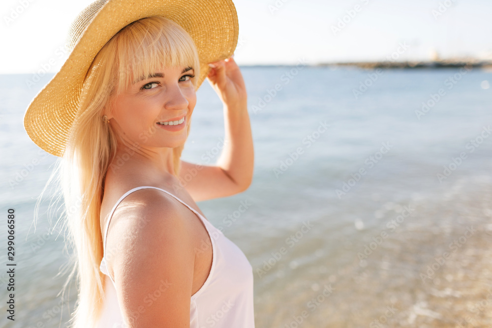 Beautiful blonde woman in hat on sunset beach