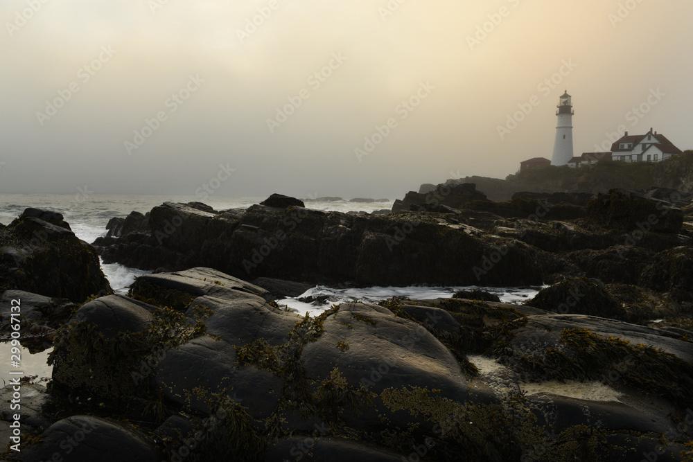 The dramatic landscape of the rocky shore and the lighthouse on the shore in the fog. USA. Maine Portland