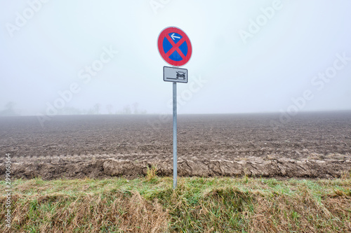 Traffic sign for absolute stopping restriction on a foggy morning in an autumnal landscape with a huge agricultural field in the background. Seen in Franconia / Bavaria in Germany in October