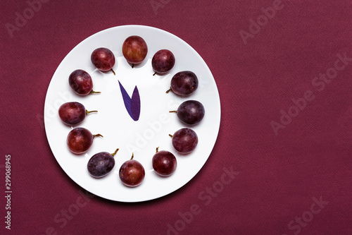 Clock of 12 piece grapes on red background. New Year concept. Spanish tradition for the new year. photo