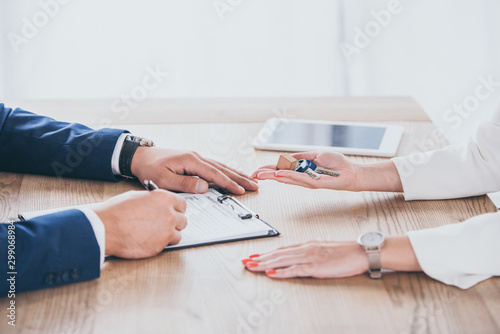 cropped view of businesswoman holding house keys near man signing agreement
