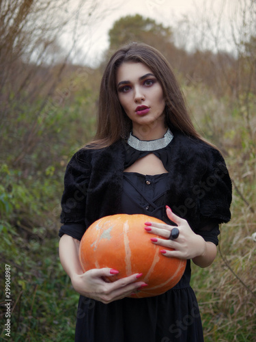Young beautiful brunette witch posing in the dreamy fall forest with pumpkin